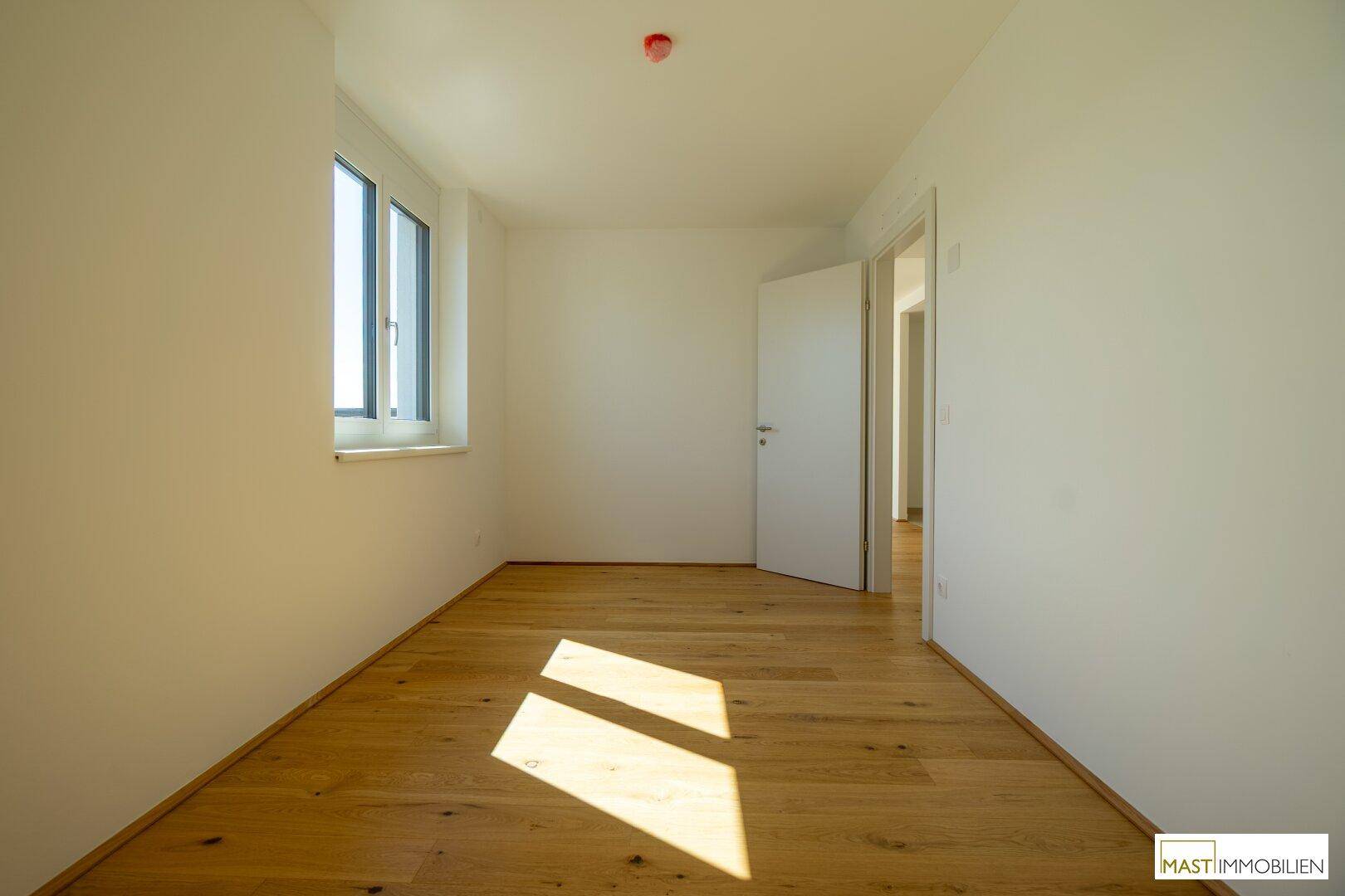 Sonniger Raum mit Holzboden und Fenster, ideal als Schlaf- oder Arbeitszimmer.