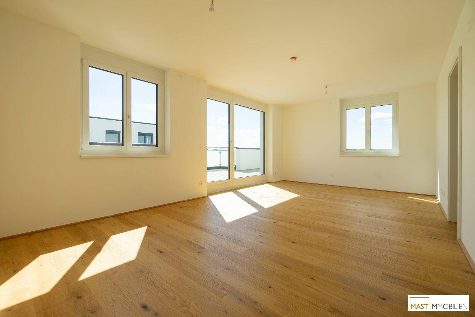 Lichtdurchfluteter Raum mit Eichenparkett und großen Fenstern, ideal als Wohnbereich.