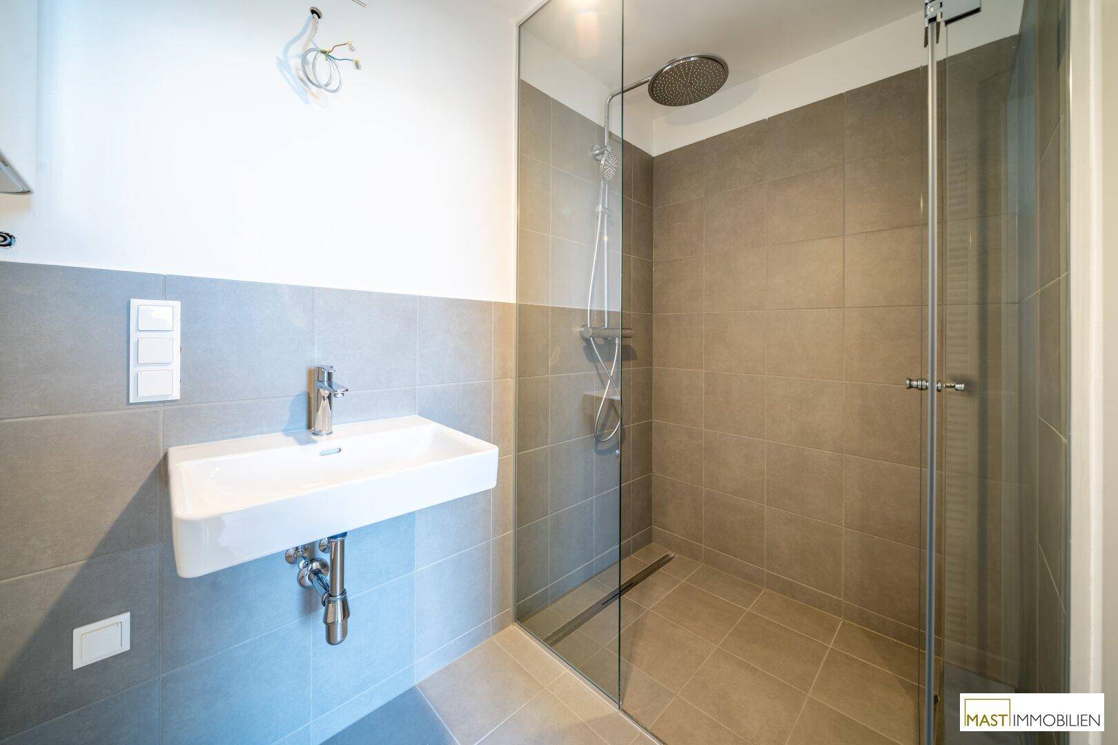 Modernes Badezimmer mit grauen Fliesen, elegantem Waschbecken und einer geräumigen Regendusche.