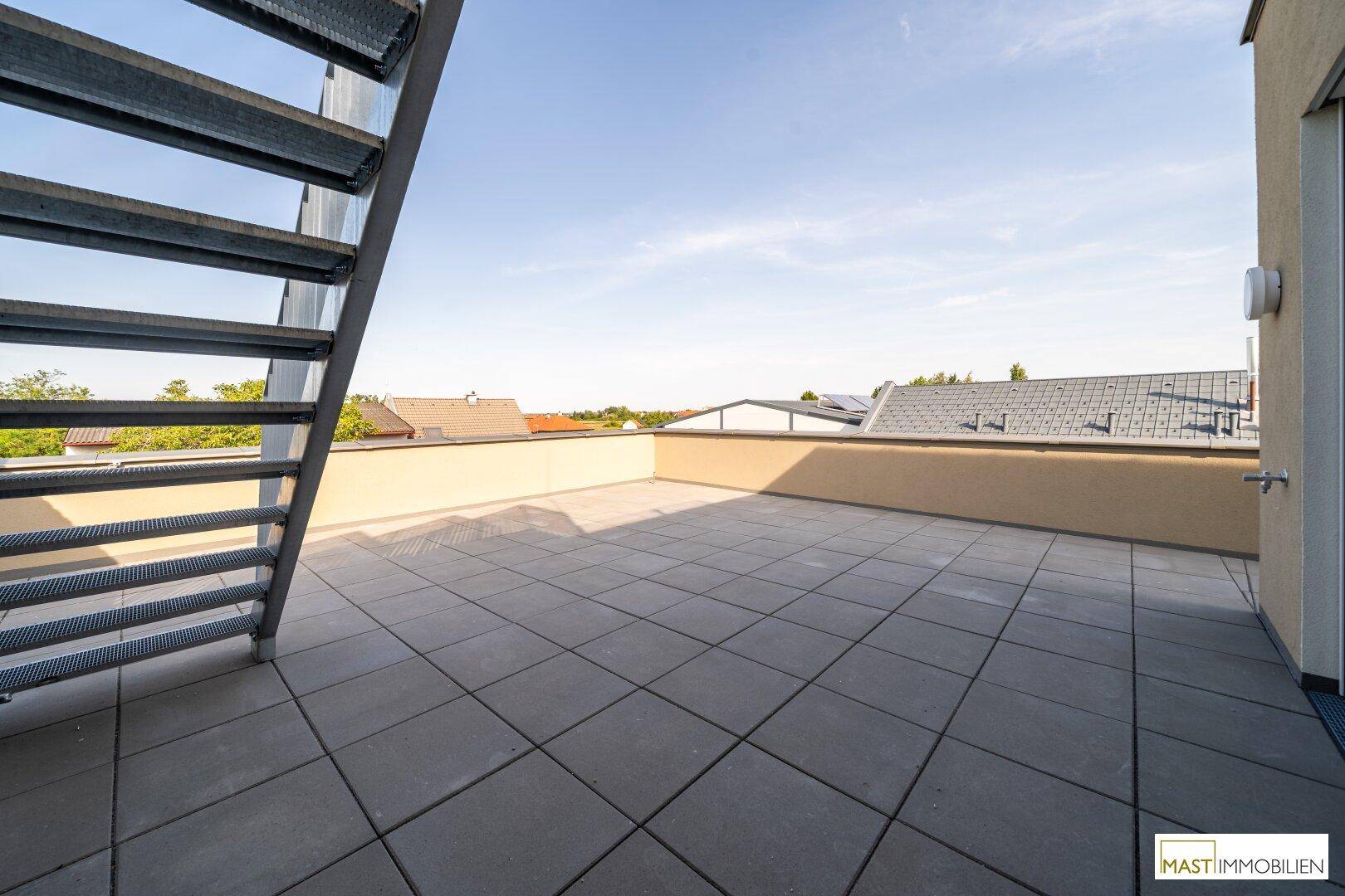 Geräumige Dachterrasse mit Fliesenboden und Metalltreppe, die einen weiten Blick bietet.