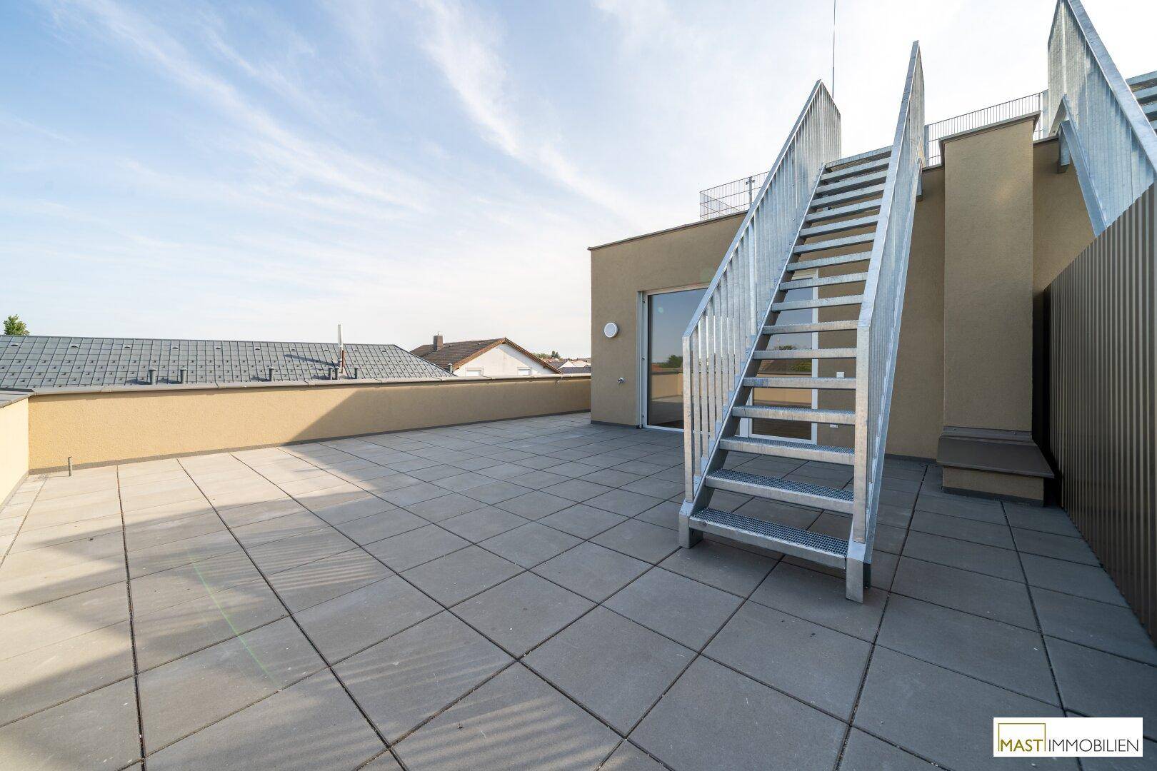Sonnige Dachterrasse mit robustem Fliesenboden und einer stabilen Metalltreppe.