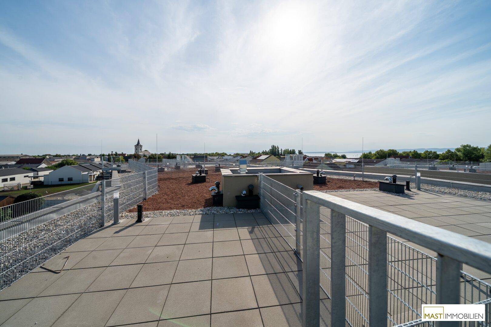 Panoramablick von der Dachterrasse über die umliegende Landschaft und einen See in der Ferne.