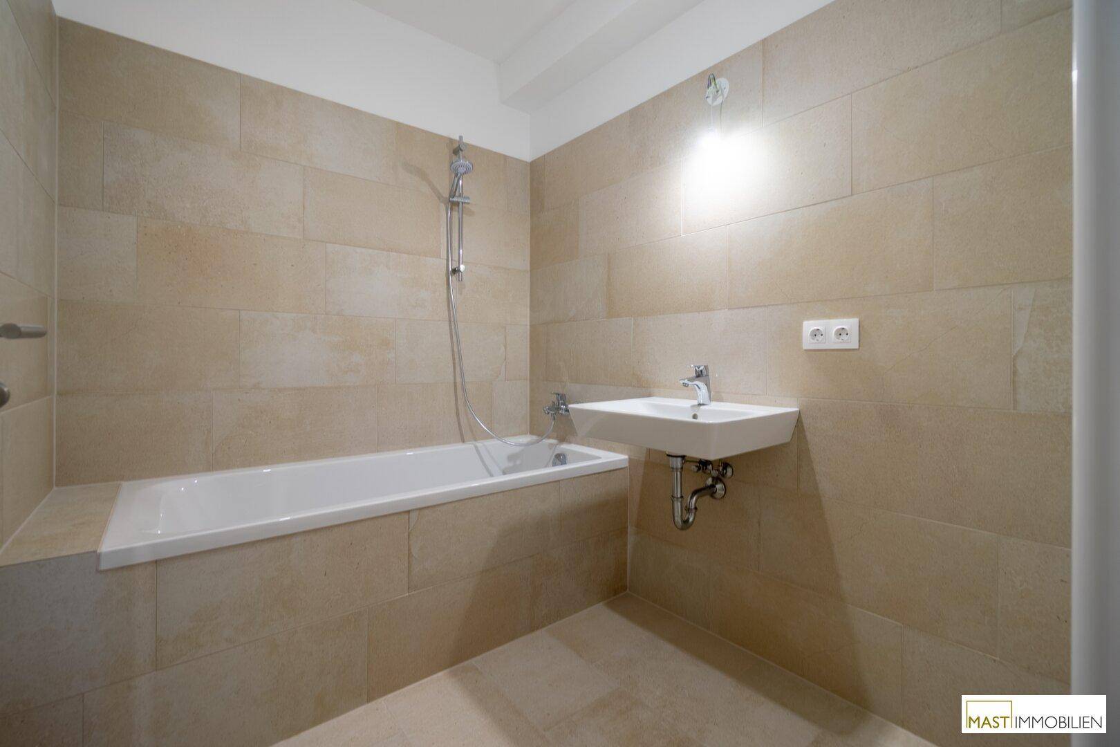 Modernes Badezimmer mit beigefarbenen Fliesen, Badewanne mit Duschfunktion und Waschbecken.