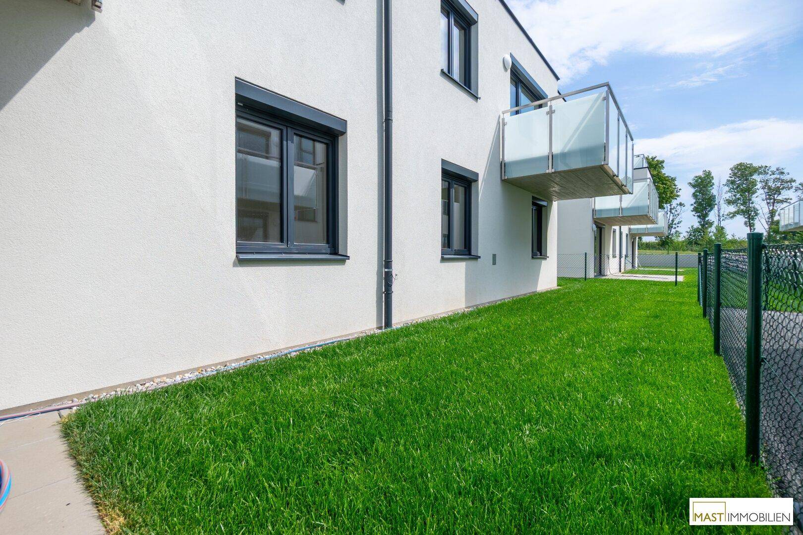 Moderne Gebäudefassade mit weißem Putz, dunklen Fenstern und einem gepflegten Rasenbereich.