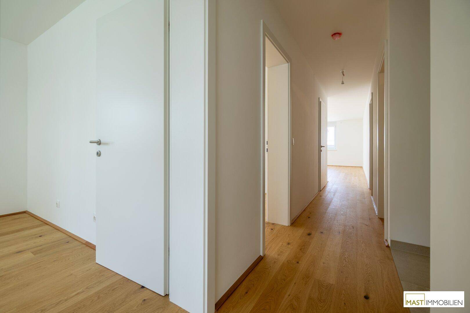 Langer, heller Flur mit Holzboden und mehreren Türen, die zu verschiedenen Räumen führen.