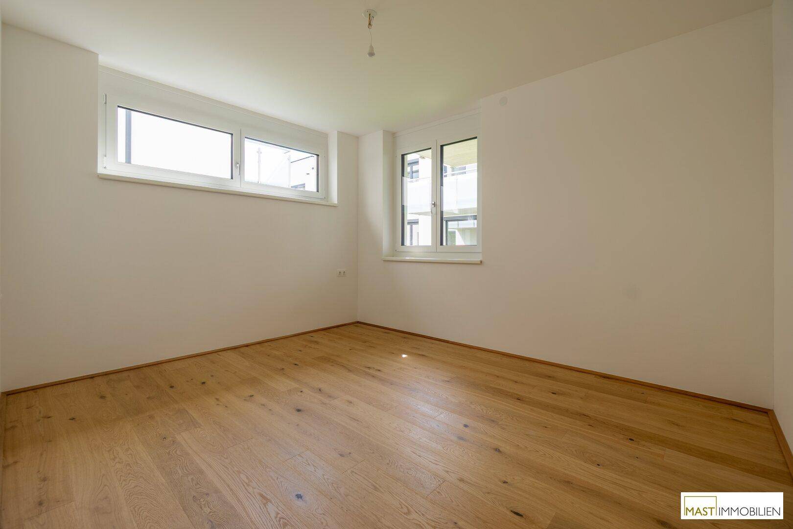 Geräumiges Zimmer mit Holzboden und zwei Fenstern, die für gute Belichtung sorgen.
