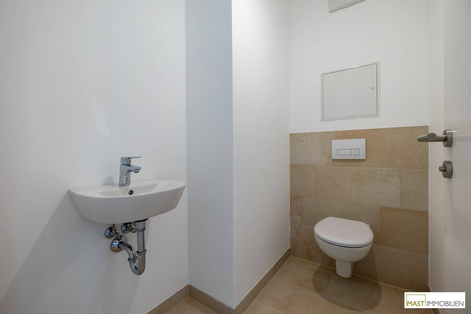 Separates Gäste-WC mit wandhängender Toilette und kleinem Waschbecken, teilweise gefliest.