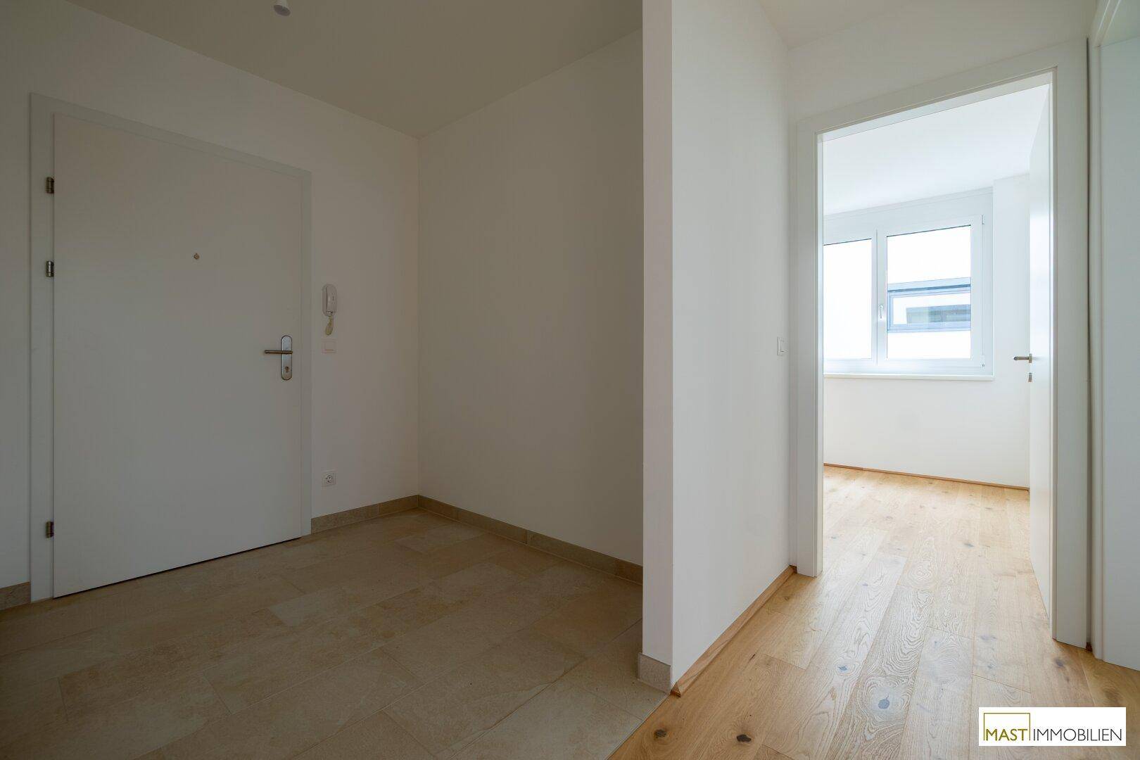 Heller Eingangsbereich mit Fliesenboden und weißer Tür, der zu weiteren Wohnbereichen führt.