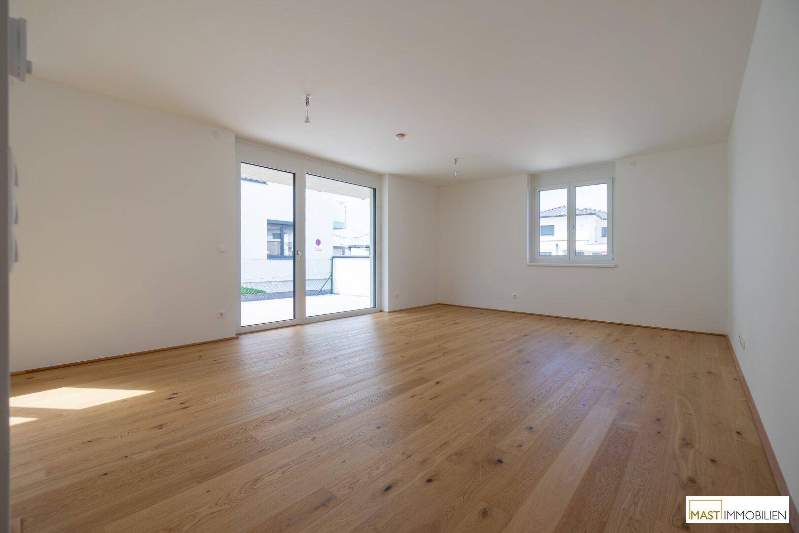 Geräumiges, helles Zimmer mit Holzboden und Zugang zu einem Außenbereich durch eine große Schiebetür.