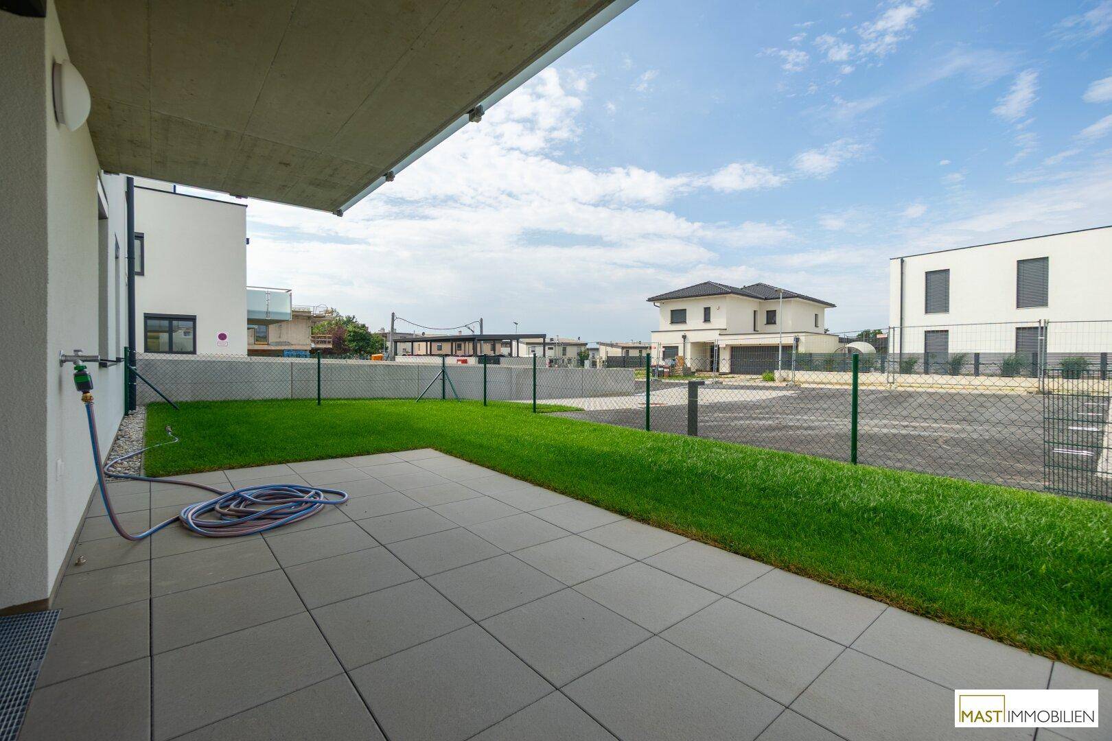 Sonniger Terrassenbereich mit Rasenfläche und Blick auf die umliegende Nachbarschaft.