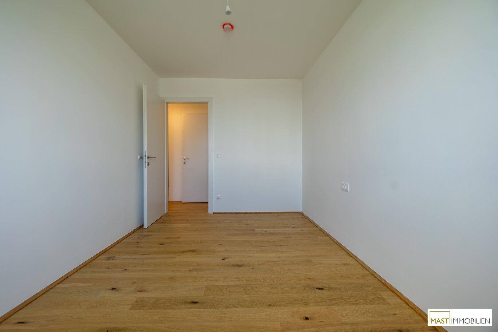 Leeres Schlafzimmer mit Holzboden und weiß gestrichenen Wänden, bietet viel Gestaltungspotenzial.