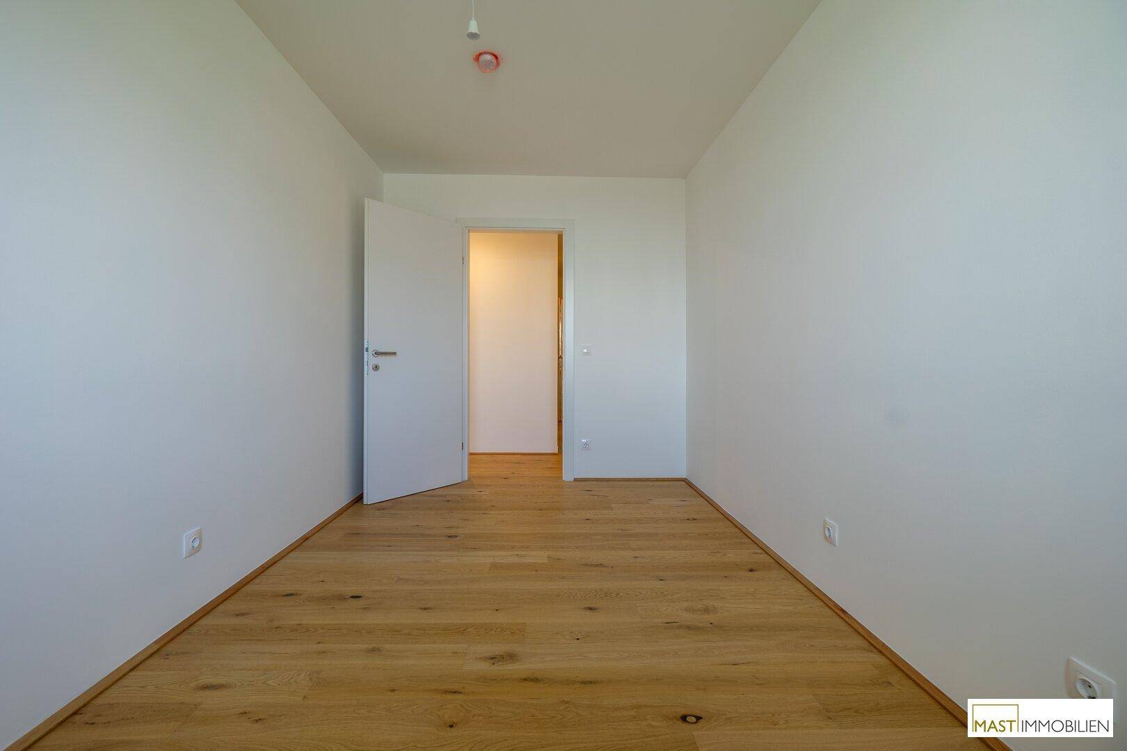 Leeres Schlafzimmer mit Holzboden und weißer Tür, bereit für Ihre persönliche Einrichtung.