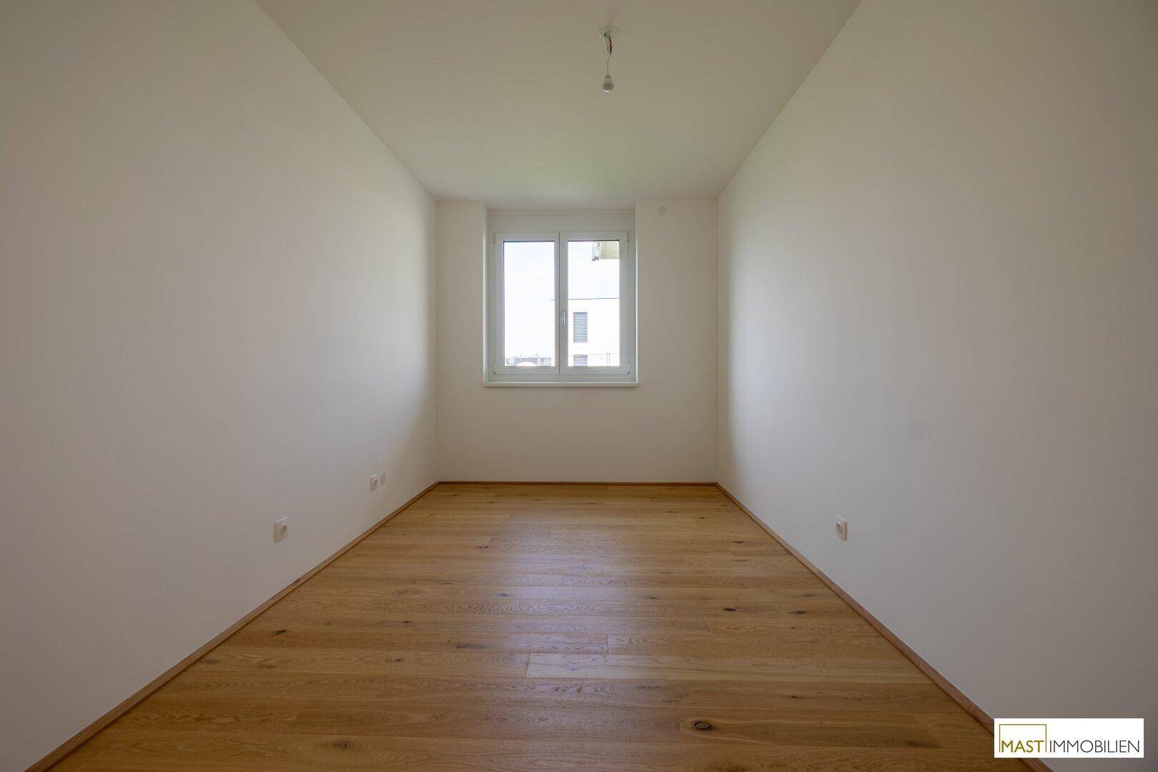 Schlichtes Schlafzimmer mit Holzboden und einem Fenster, ideal als Kinder- oder Gästezimmer.