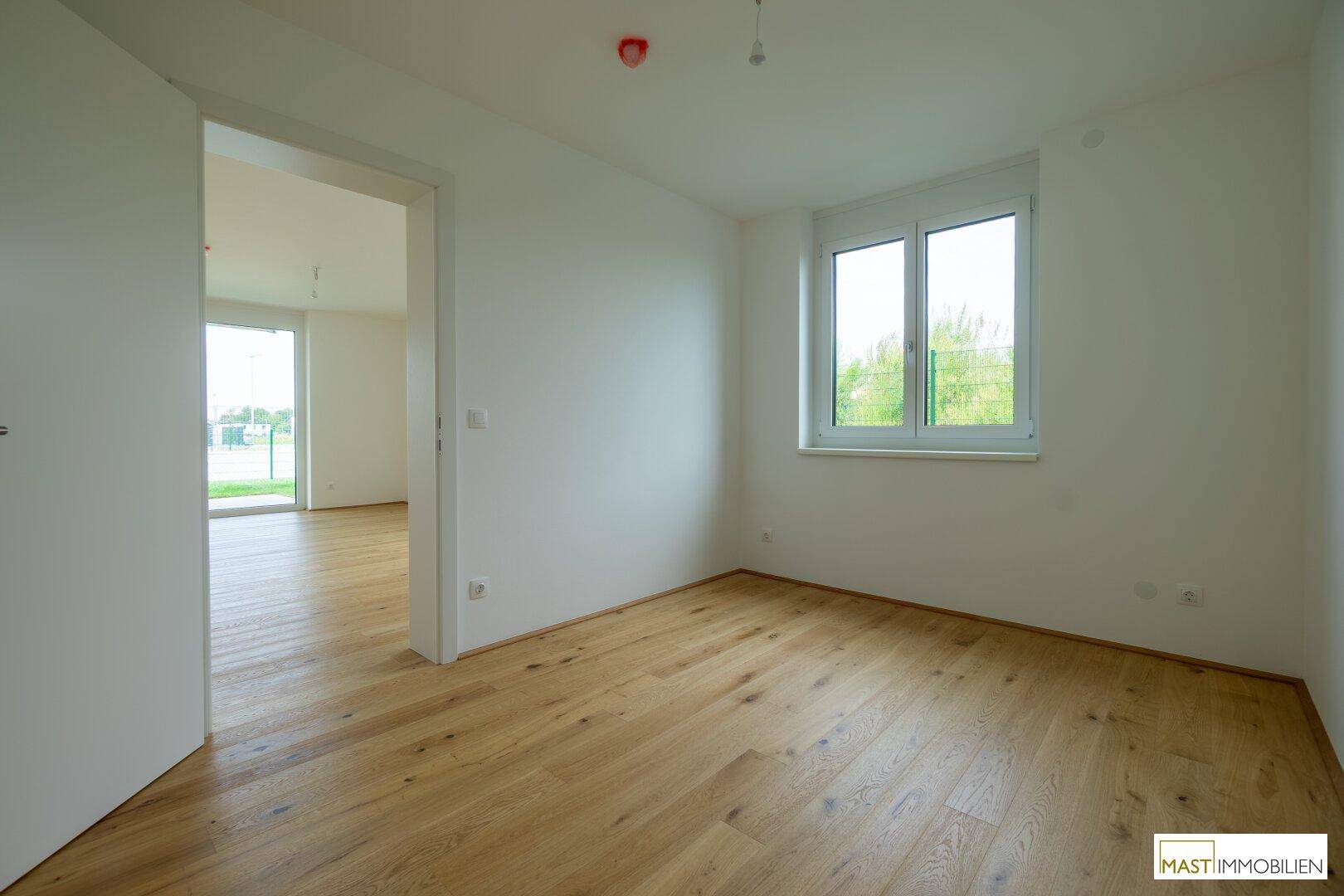 Helles Schlafzimmer mit Holzboden und Fenster mit Blick ins Grüne, bereit zum Einzug.
