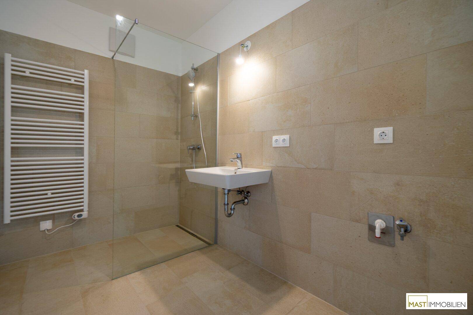 Modernes Badezimmer mit beigefarbenen Fliesen, ebenerdiger Dusche und beheiztem Handtuchhalter.