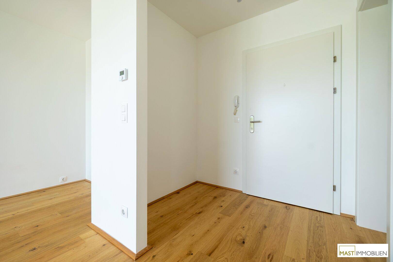 Heller Eingangsbereich mit Holzboden und einer modernen weißen Wohnungstür, die zum Flur führt.