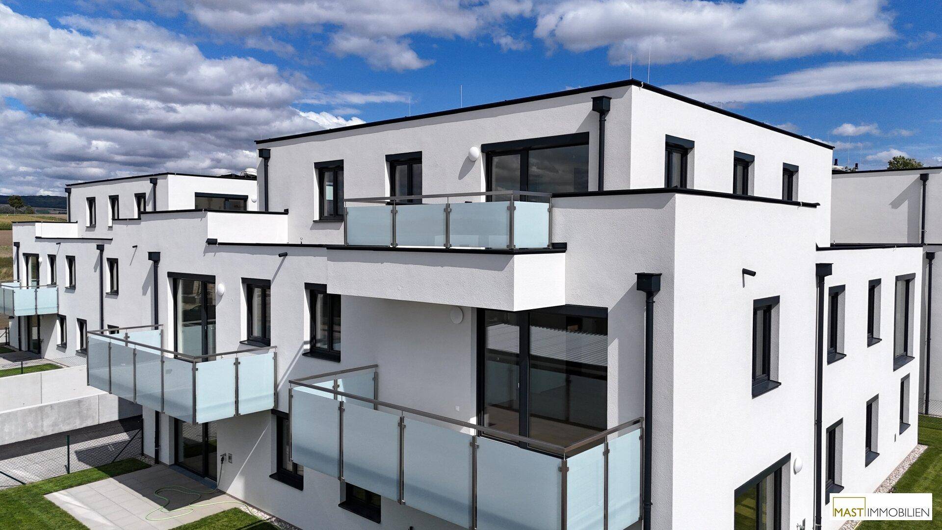 Nahaufnahme der modernen Fassade eines Wohngebäudes mit weißen Wänden und Glasbalkonen.