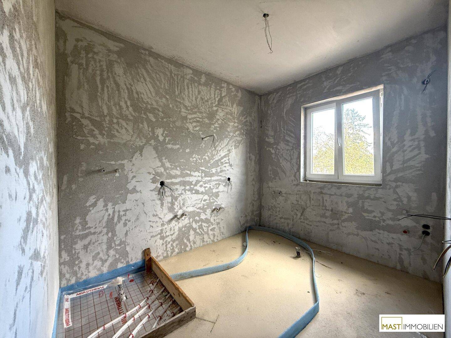 Rohbau-Raum mit sichtbaren Unterputzinstallationen und Fenster, vorbereitet für den Ausbau.