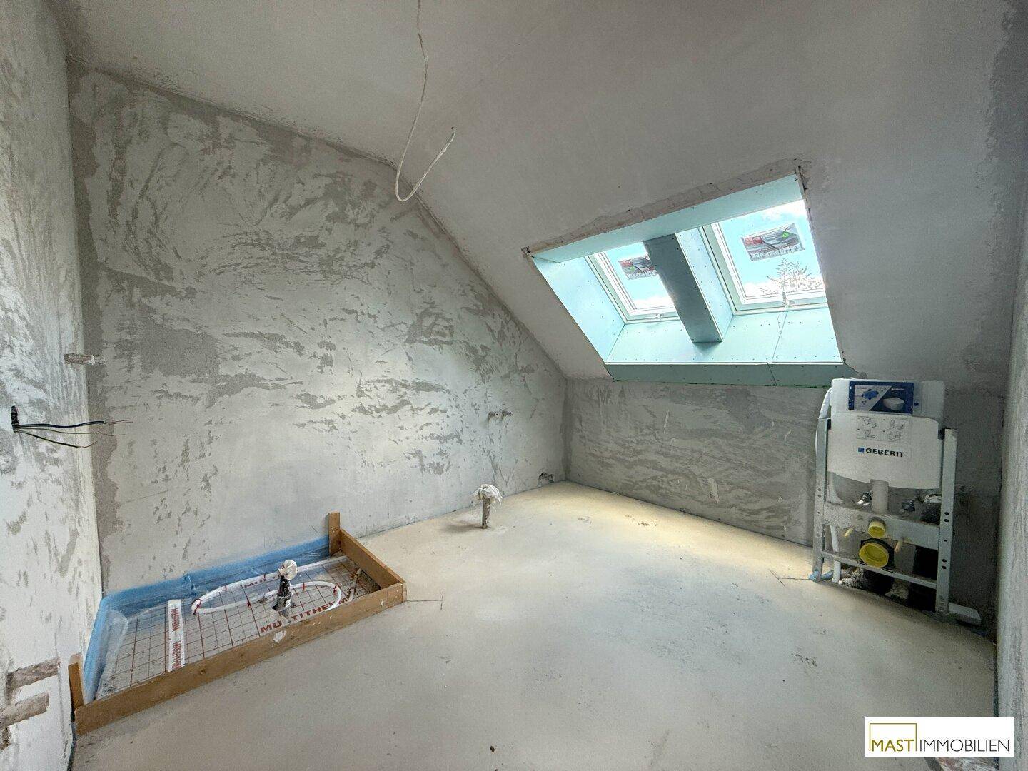 Rohbau-Badezimmer im Dachgeschoss mit Dachfenster und sichtbaren Sanitärinstallationen.