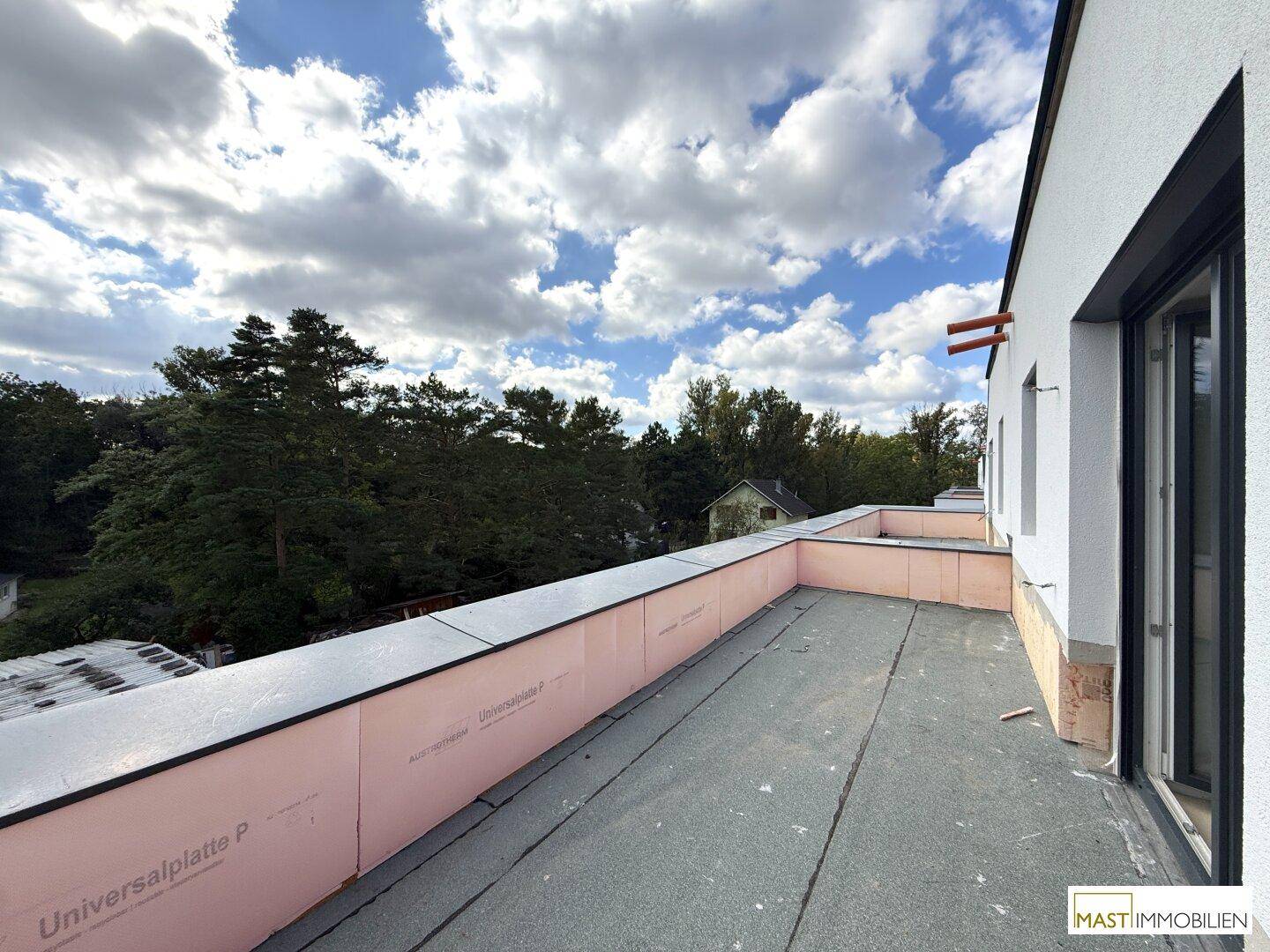 Unfertige Dachterrasse mit Blick auf grüne Bäume und den Himmel, bereit für die Gestaltung.