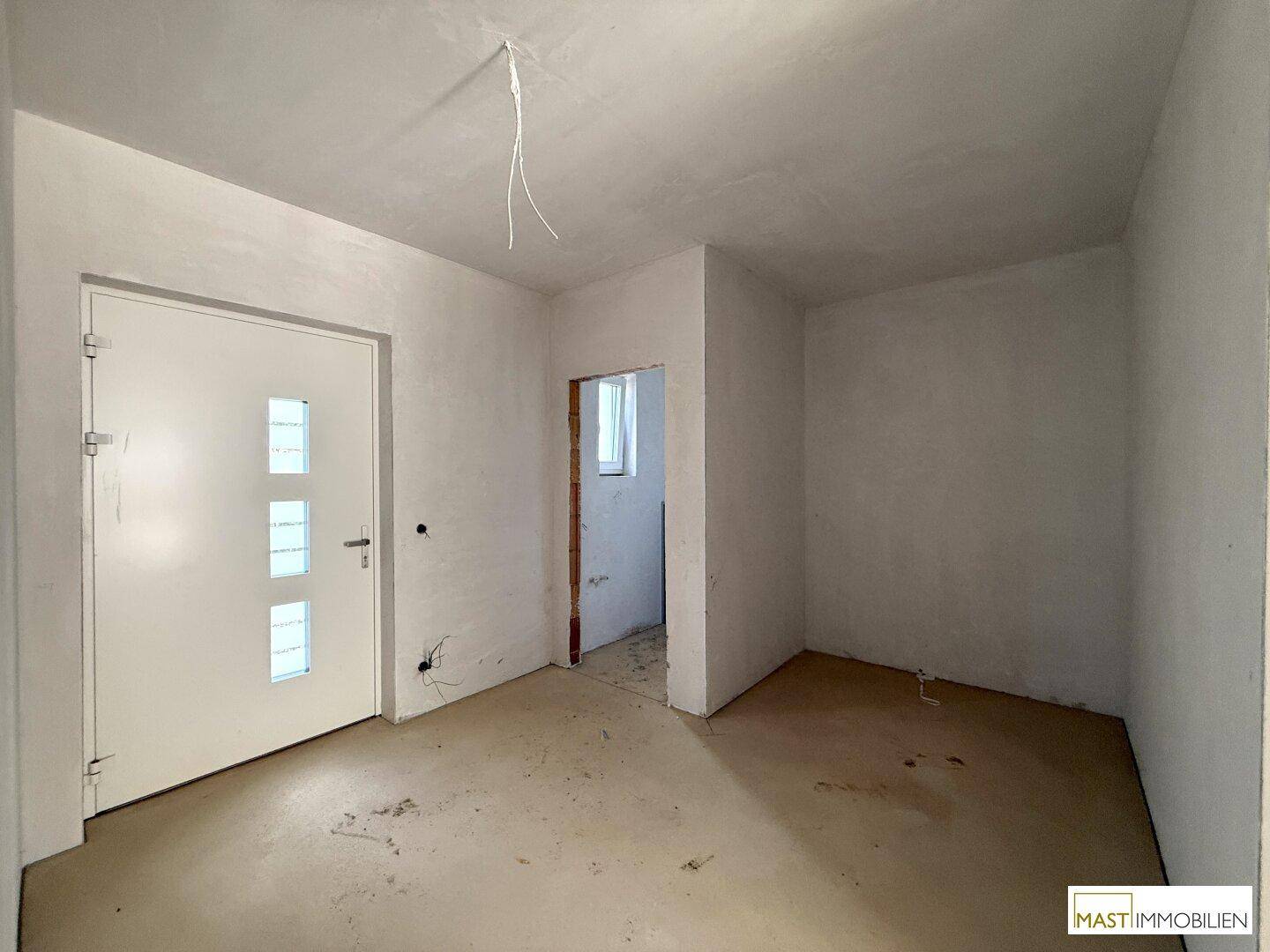 Eingangsbereich im Rohbauzustand mit weißer Tür und vorbereiteten Wänden für den Innenausbau.