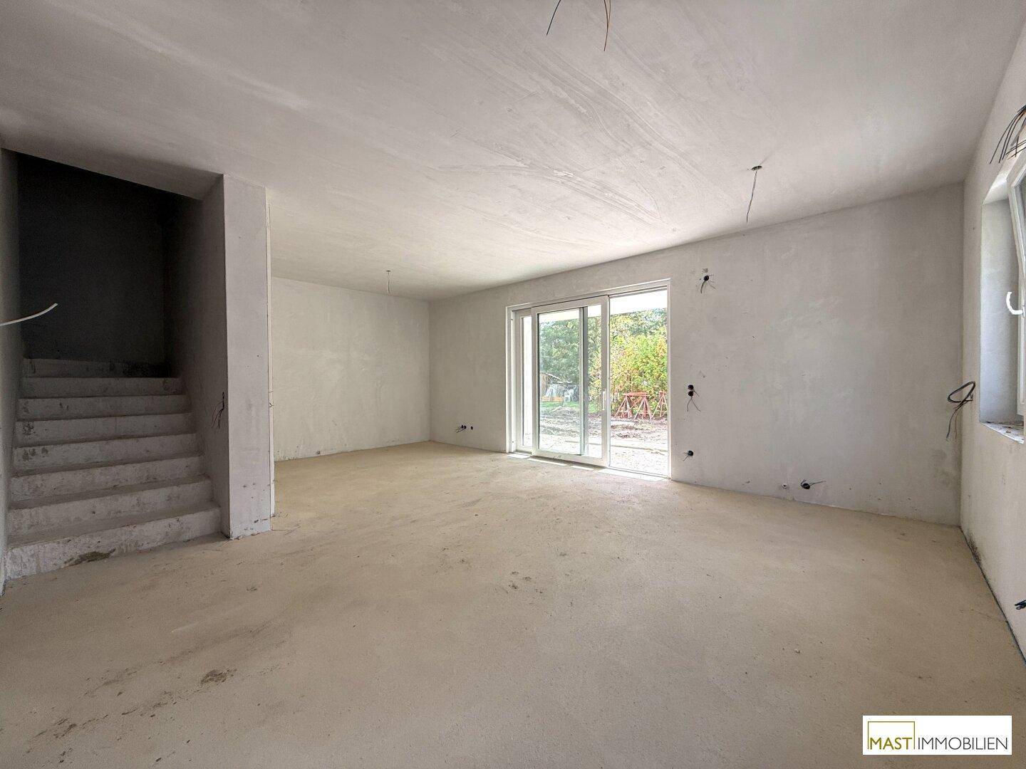 Heller Rohbau-Wohnraum mit Betontreppe und großer Schiebetür zum zukünftigen Außenbereich.