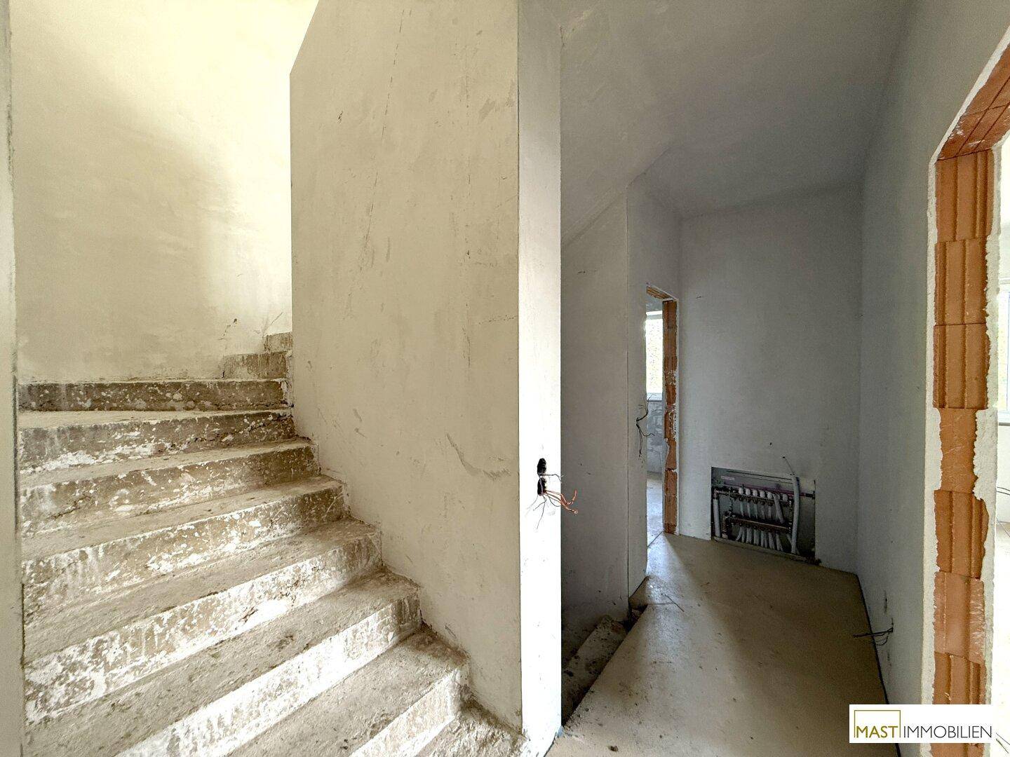Rohbau-Treppenhaus mit Betonstufen und vorbereiteten Wänden für den weiteren Innenausbau.