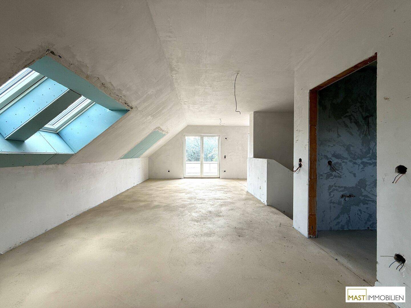 Heller Dachboden im Rohbau mit Dachfenstern und Zugang zu einem Balkon.
