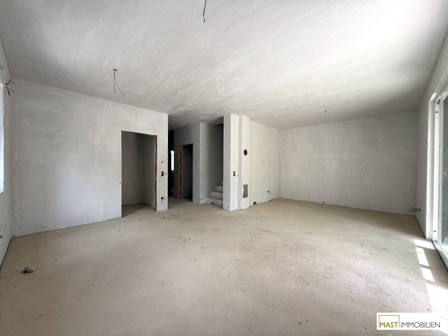Weitläufiger Rohbau-Wohnbereich mit viel Tageslicht und vorbereiteten Installationen.
