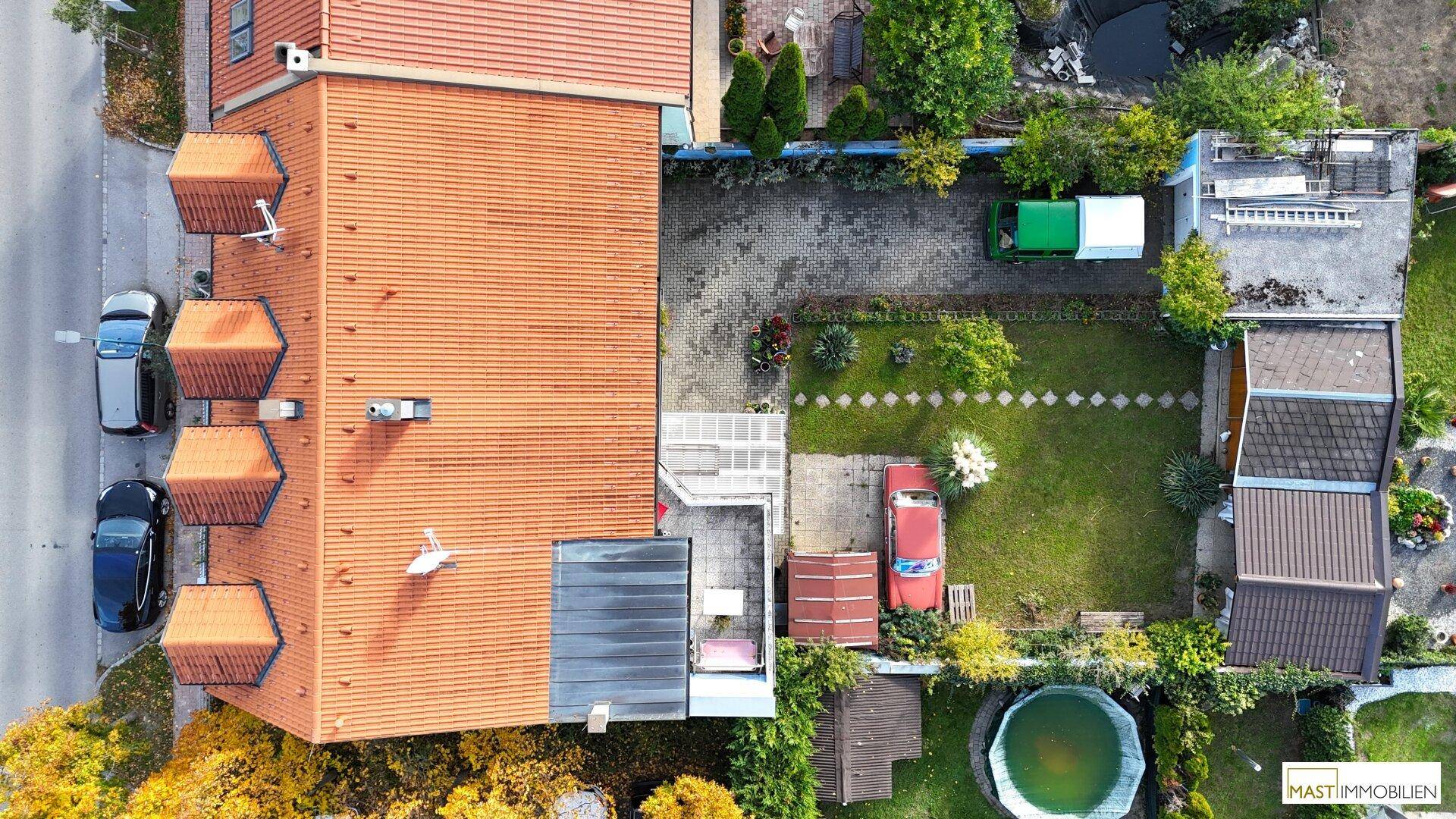 Luftaufnahme des Gartens mit Rasenfläche, Bäumen, gepflasterter Einfahrt und kleinem Pool.