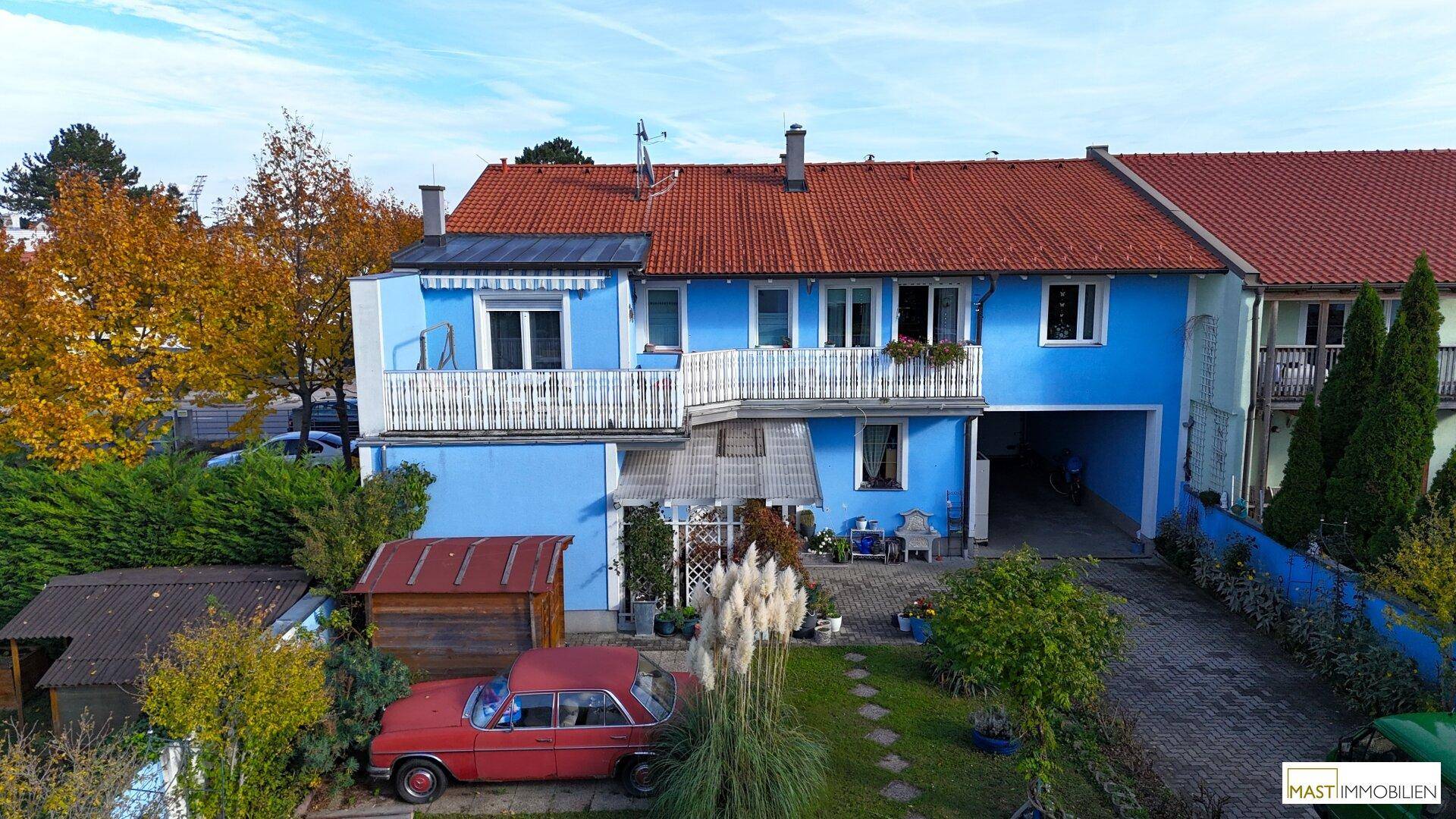 Rückansicht des blauen Reihenhauses mit Garten, Terrasse und einem alten roten Auto im Hof.