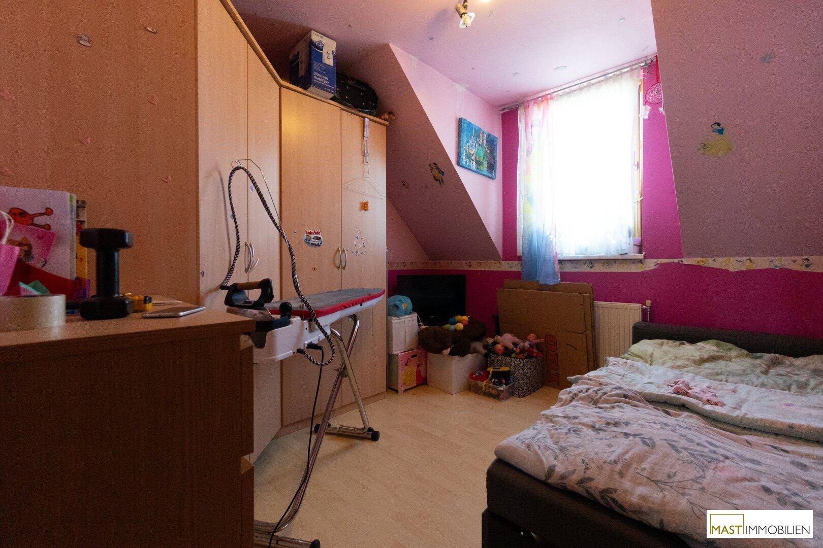 Schlafzimmer mit rosa Wänden, Dachschräge, Holzboden und einem großen Kleiderschrank.