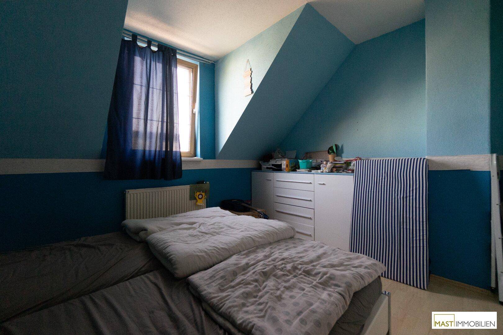Schlafzimmer mit blauen Wänden, Dachschräge, Einzelbett und Fenster.