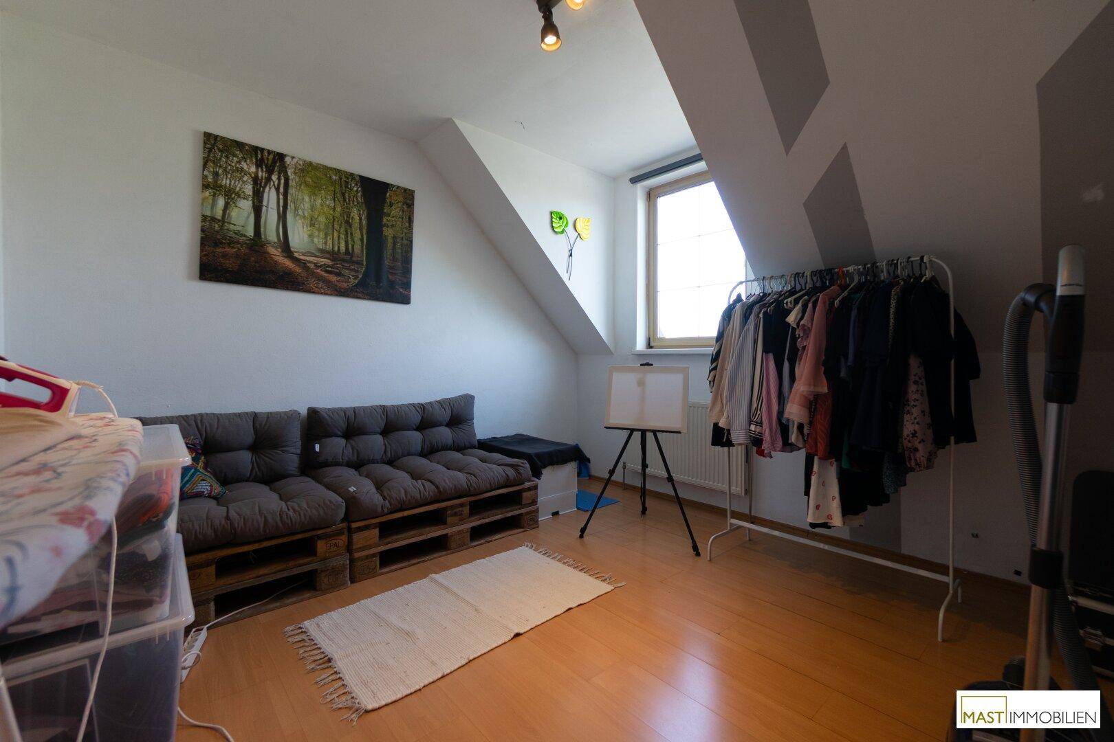 Dachzimmer mit Holzboden, Dachschräge, Sofa aus Paletten und Kleiderstange.
