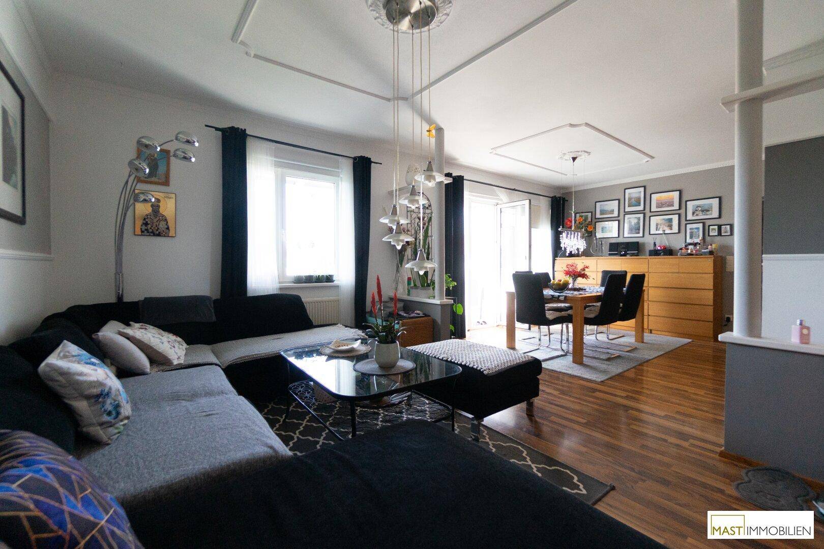Geräumiger Wohn- und Essbereich mit dunklem Sofa, Holzboden und vielen gerahmten Bildern an der Wand.