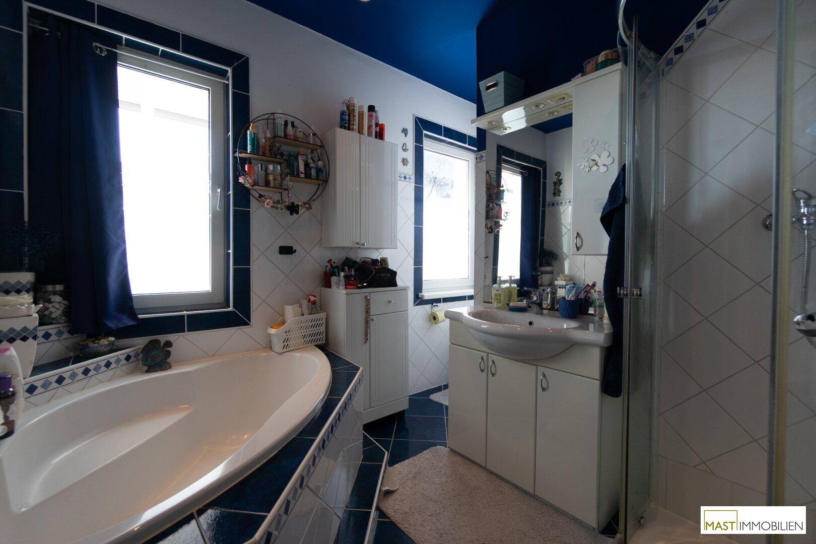 Blau-weiß gefliestes Badezimmer mit Badewanne, Dusche und Fenster.