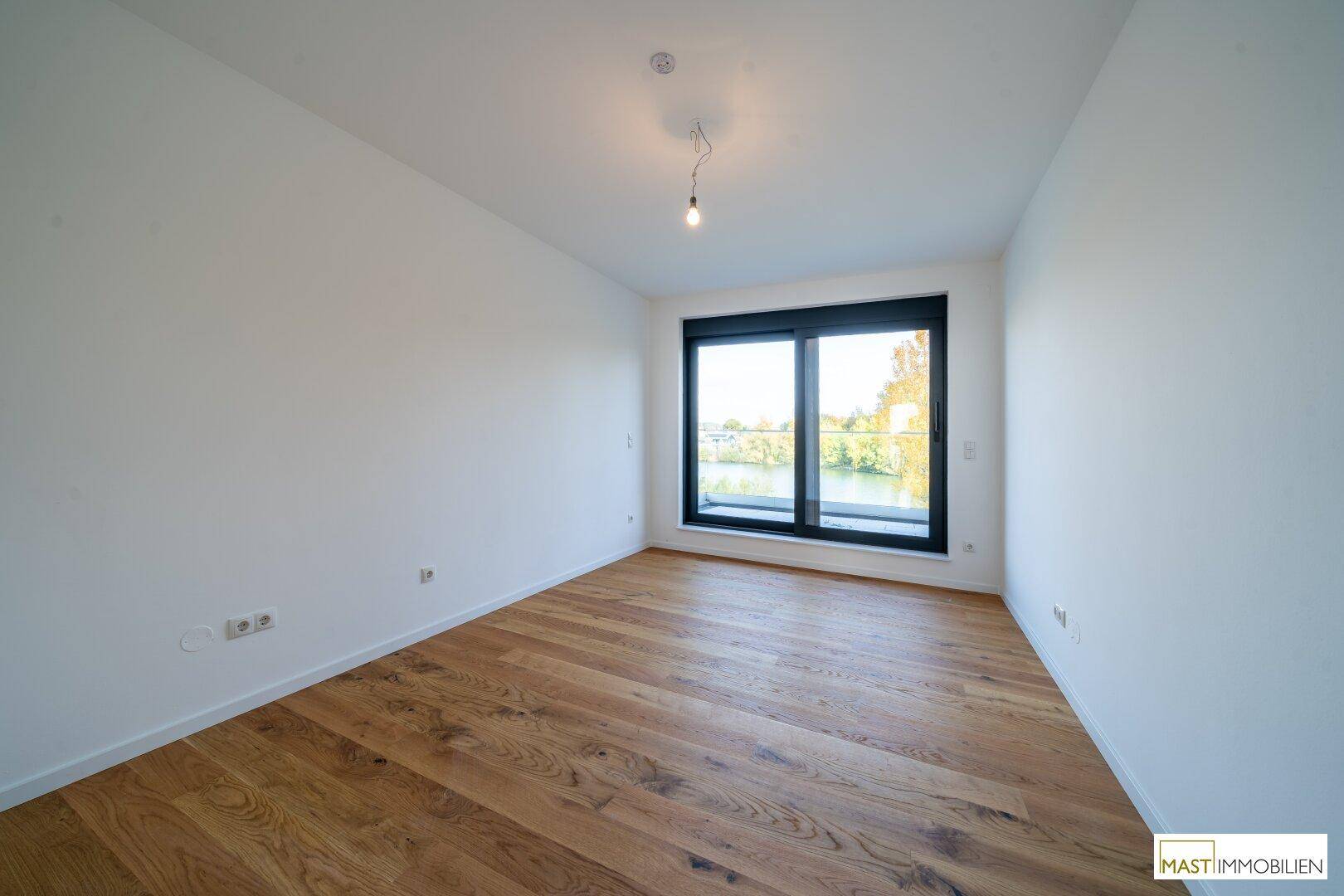 Helles Schlafzimmer mit Holzboden und großem Fenster, das einen schönen Seeblick bietet.