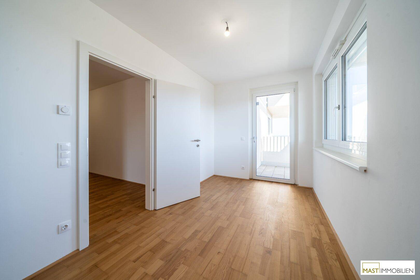 Helles Zimmer mit Parkettboden und direktem Zugang zu einem Balkon, ideal als Schlaf- oder Arbeitszimmer.