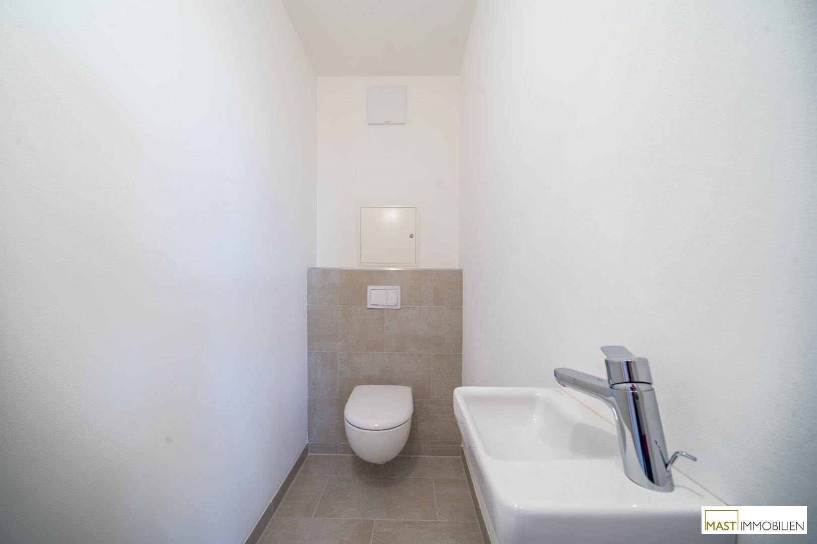 Gäste-WC mit wandhängender Toilette, kleinem Waschbecken und modernen Fliesen im unteren Bereich.