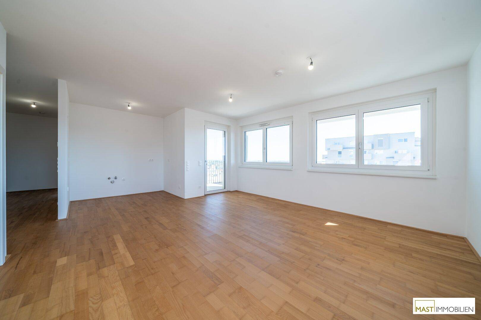 Lichtdurchfluteter Wohnraum mit Parkettboden und Zugang zu einem Balkon, ideal für offenes Wohnen.