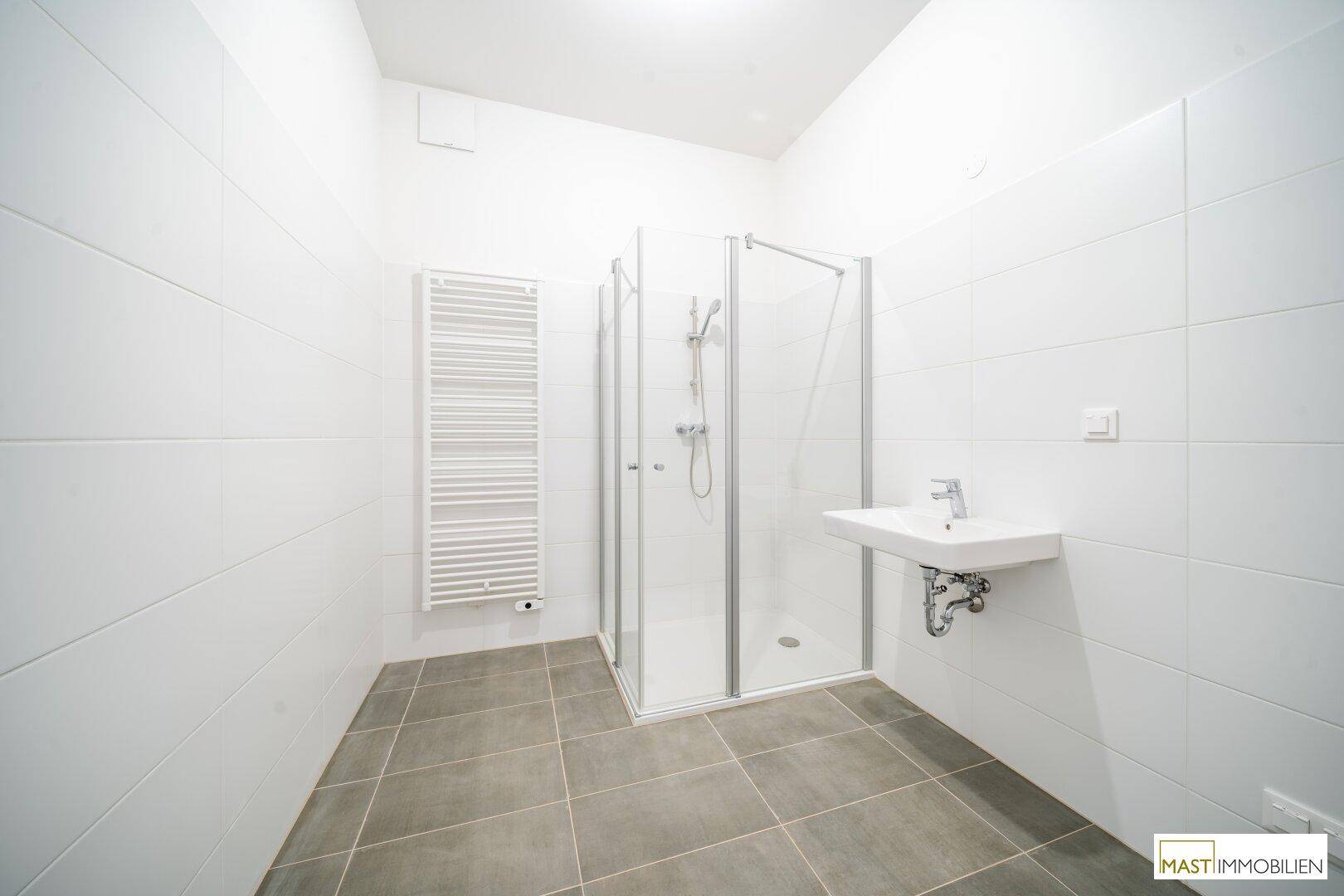 Modernes Badezimmer mit weißen Fliesen, ebenerdiger Dusche, Waschbecken und beheiztem Handtuchhalter.