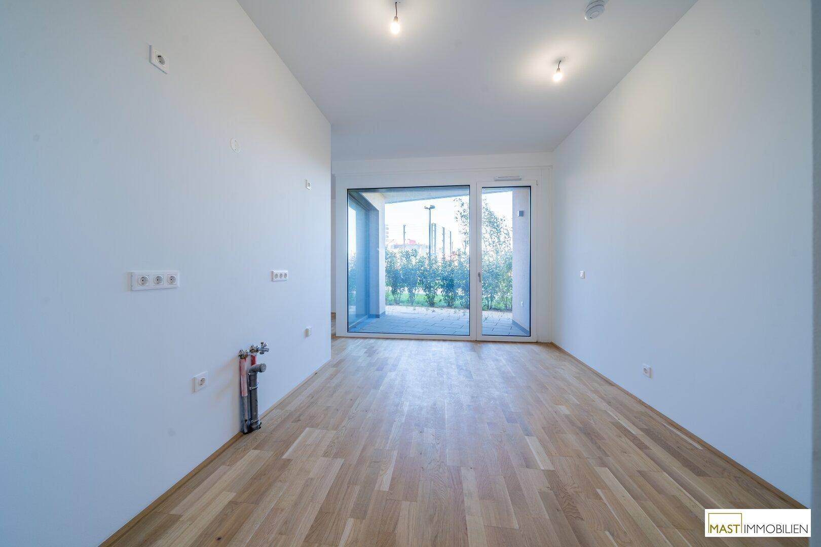 Geräumiger, heller Raum mit Parkettboden, großen Fenstern und Anschlüssen für eine mögliche Küche.