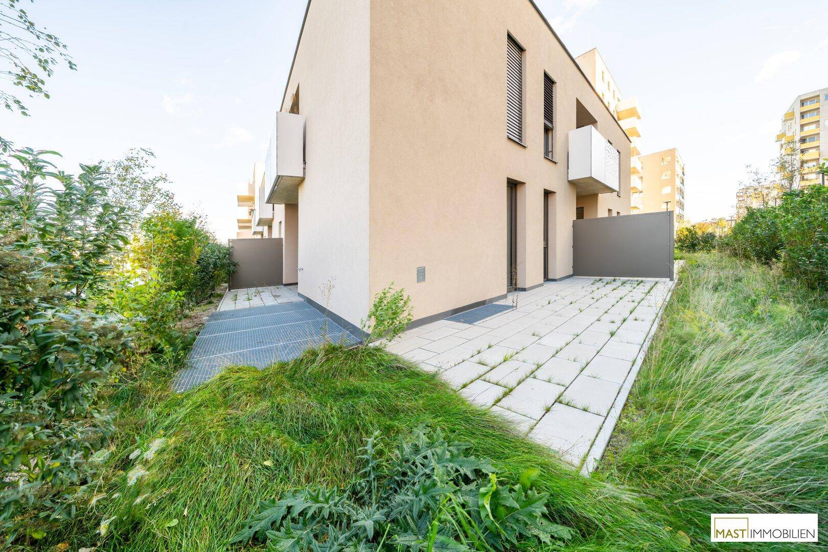 Außenansicht des modernen Gebäudes mit einer gepflegten Rasenfläche und einer kleinen gepflasterten Terrasse.
