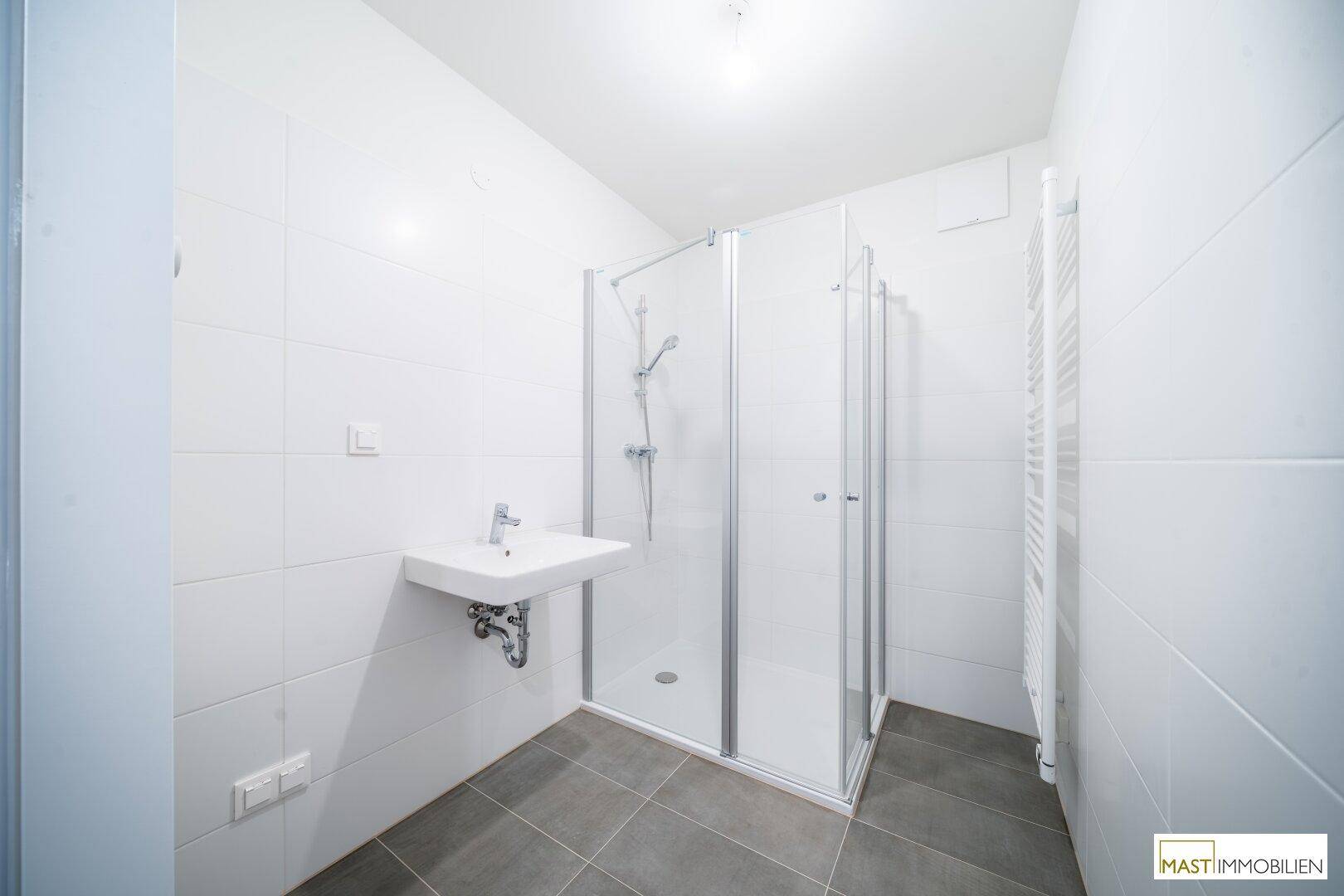 Modernes Badezimmer mit weißen Wandfliesen, grauen Bodenfliesen, Dusche und Handtuchheizkörper.