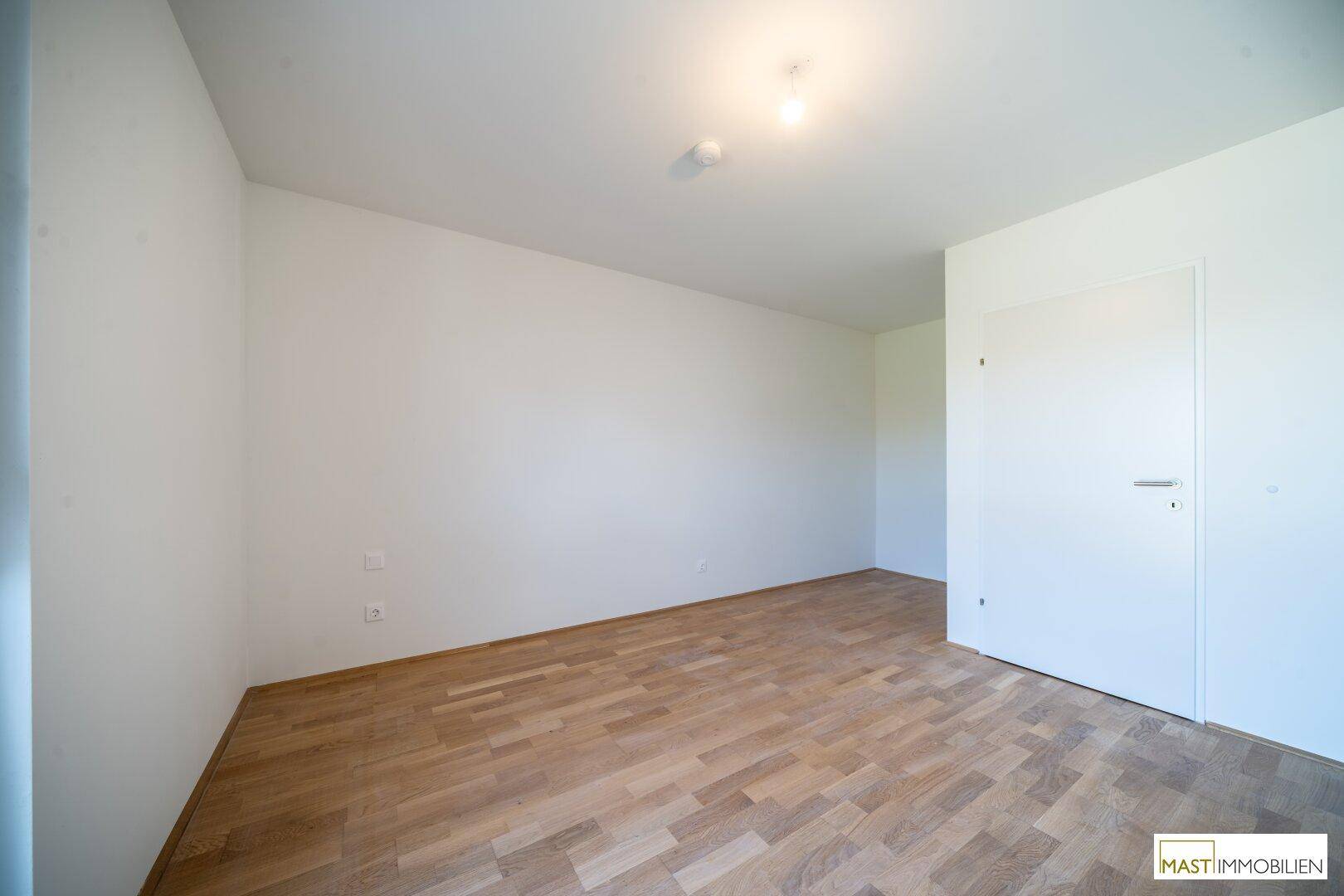 Leeres Zimmer mit Parkettboden und weißen Wänden, ideal als Schlafzimmer oder Arbeitszimmer.