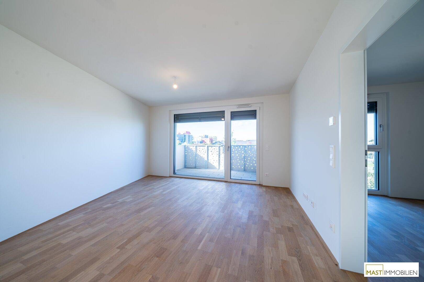 Heller Raum mit Parkettboden und Zugang zu einem Balkon durch eine große Schiebetür.