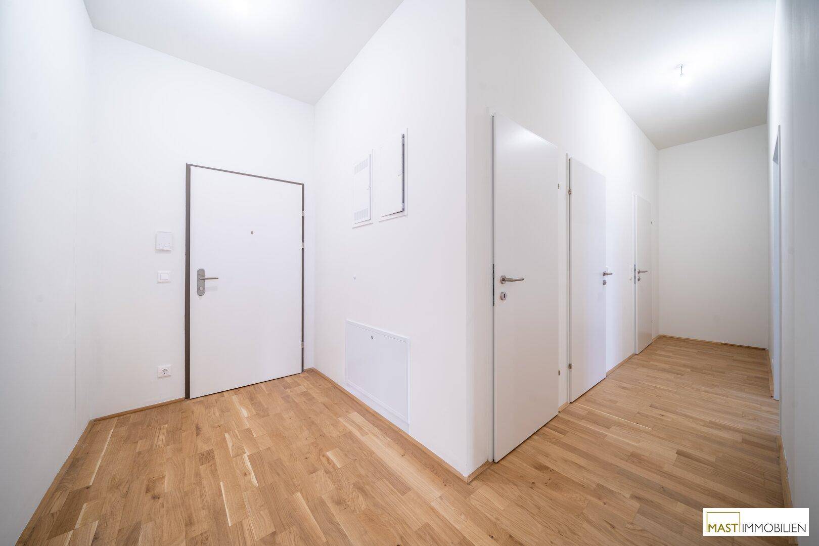 Heller Flur mit Holzboden und mehreren weißen Türen zu den Zimmern.