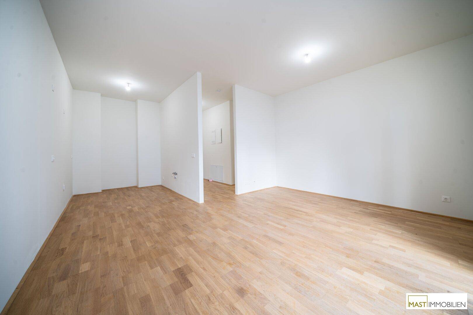 Großer, heller Raum mit Parkettboden, teilweise durch eine Wand geteilt.