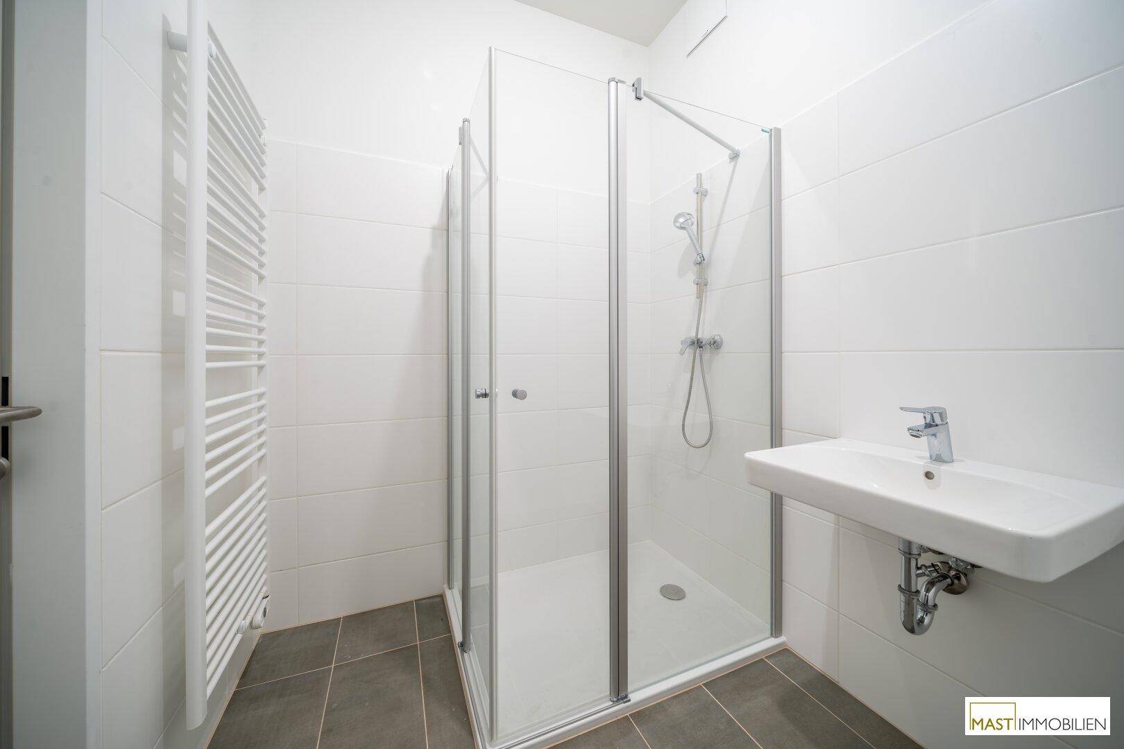 Modernes Badezimmer mit Duschkabine, Waschbecken und beheiztem Handtuchhalter.