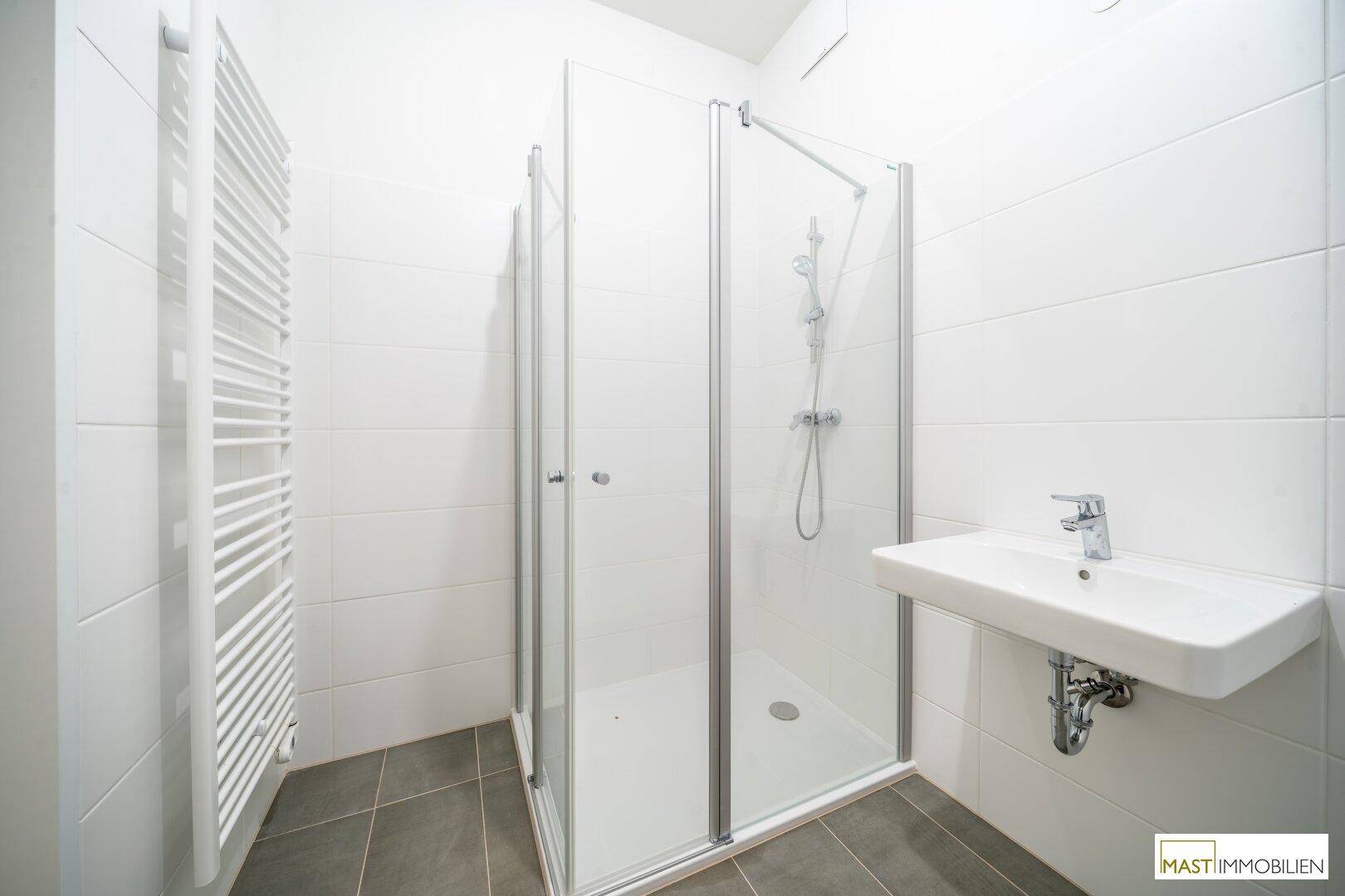 Modernes Badezimmer mit weiß gefliesten Wänden, Duschkabine und beheiztem Handtuchhalter.